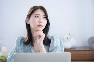 部屋でパソコンをみて考える悩む迷うかわいい女性　ちょっと真剣なネガティブイメージ　転職どうしようかな～
