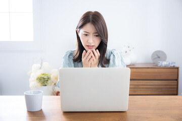 部屋でパソコンをみて考える悩む迷うかわいい女性　ちょっと真剣なネガティブイメージ　驚くビックリする表情
