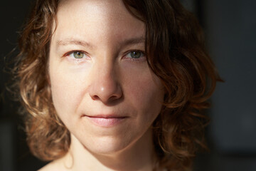 Caucasian female adult with curly hair in soft light close-up portrait.