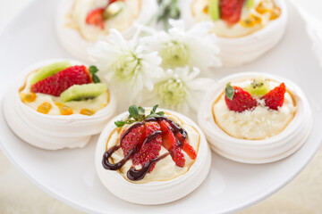 Mini Pavlova desserts topped with fruit on a white plate