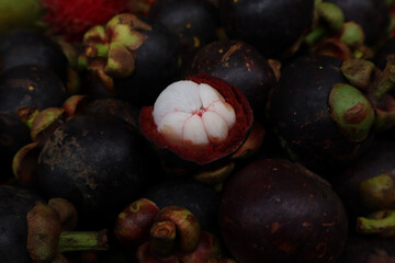 A pile of ripe mangosteens, with one prominently opened to reveal its white, segmented flesh. The...