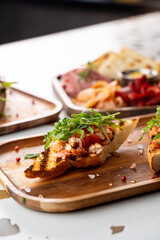 Delicious bruschetta adorned with vibrant tomatoes and peppery greens sits elegantly on a wooden platter. Lively atmosphere surrounds the gourmet meal as patrons enjoy the culinary delights
