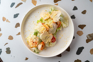Vibrant caesar salad served on a decorative plate showcases fresh greens topped with succulent shrimp and crispy textures. Perfect for a midday indulgence in a bustling eatery