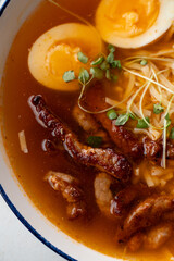 A warm, inviting bowl filled with rich, flavorful broth surrounds tender slices of pork and boiled eggs, garnished with fresh sprouts. Perfect for a chilly night, enticing aromas fill the air