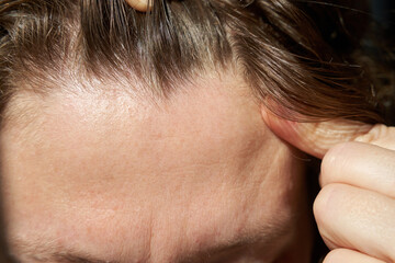 Close-up of young caucasian female showing scalp with light brown hair and healthy skin detail.