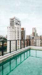Vertical photo of a rooftop swimming pool with São Paulo skyline view