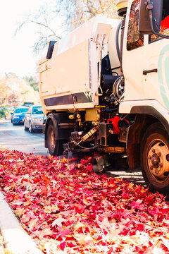 street sweeper clearing autumn leaves on the side of a road