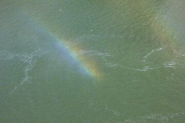 Rainbow appears above shimmering water in a serene natural setting during daylight hours
