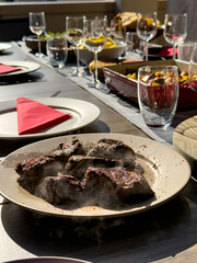Meat dish on a beautifully set brunch table with salad, bread, vegetables, and drinks, under warm natural sunlight. Elegant and inviting.