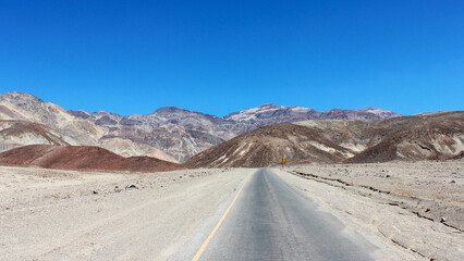 Open road stretches through arid landscape with distant mountains under clear blue sky in a desert location