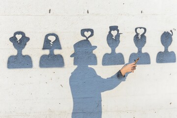 Shadowed figure photographing graffitied human profiles on a wall.