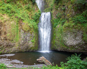Multnomah waterfall cascades into serene pool surrounded by lush greenery in a tranquil natural setting