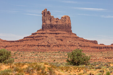 Monument Valley features red rock formations beneath a blue sky in a sunny afternoon landscape in...