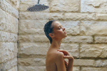 young woman enjoying refreshing outdoor shower under rainfall, relaxed pose, natural stone wall background, wet skin glistening in soft light