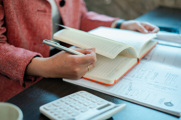 Close-up of a person writing in a planner with a calculator, focusing on financial planning and organization.
