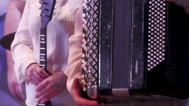 Musicians stand on stage holding accordion and domra musical instruments. Close-up.