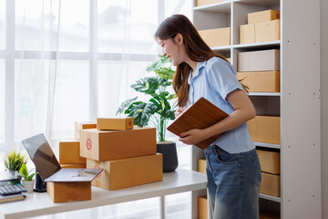 Asian woman entrepreneur taking notes while working on laptop a customer managing orders in her sme small business store. sme supply chain, procurement, omnichannel or coronavirus quarantine concept.
