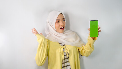 Asian Muslim woman wearing yellow cardigan and hijab surprised looking at green phone screen on...