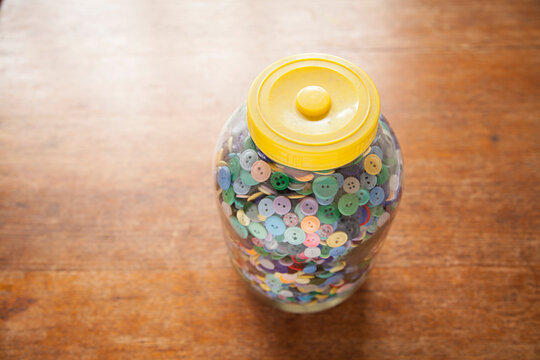 A Large jar of buttons sitting on a wooden table