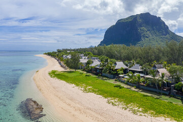 Aerial view of luxury beachfront villas beneath dramatic Le Morne Brabant mountain in Mauritius....
