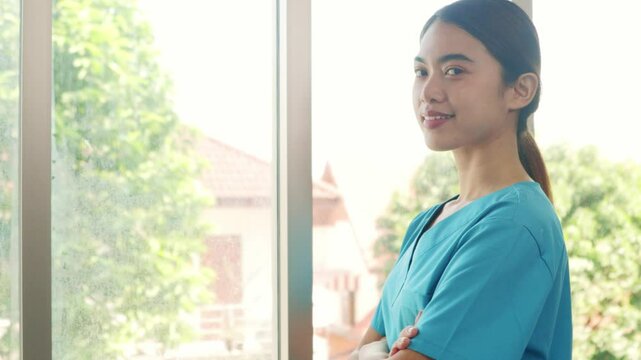 Portrait asian female doctor in blue uniform happy in nursing work in hospital smiling at camera standing with arms crossed while working in hospital.