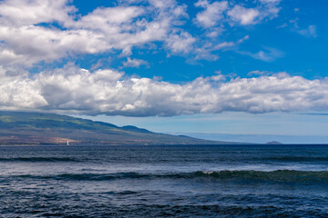 Ocean view of Maui with blue sky and clouds, and a sailboat.