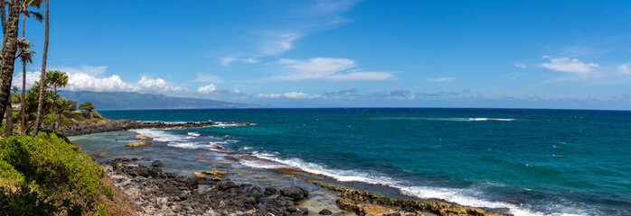 Panoramic view of a rocky beach with turquoise water and a blue sky.