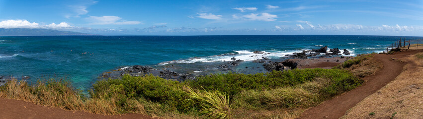 Panoramic view of a tropical coastline with a dirt path and lush vegetation.