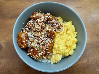A bowl of rice with scrambled egg, chicken cubes and sesame seed