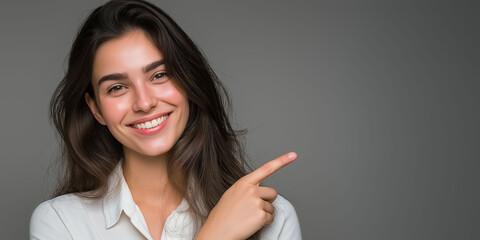 Portrait of a beautiful, smiling  latin woman pointing her finger to the side against a grey background, with space for text, suitable for an advertising banner or poster. 