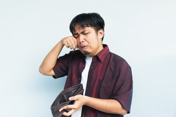 Asian Indonesian man showing his empty wallet with sad and worried expression. Isolated in gray...