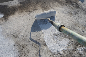 Painter applying a fresh white waterproof coat paint with a roller tool to a roof surface. POV.