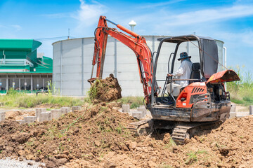 The mini excavator is scooping the stockpiled soil to backfill the piles.