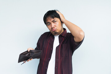 Asian Indonesian man showing his empty wallet with sad and worried expression. Isolated in gray background.