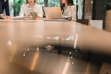A group of three young busineewoman are sitting at a desk with documents, tablet, laptop, and other equipments. They are having a discussion and planning session to improve the company.