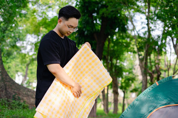 Man setting up a picnic in a green park while folding a yellow checkered blanket against a backdrop...