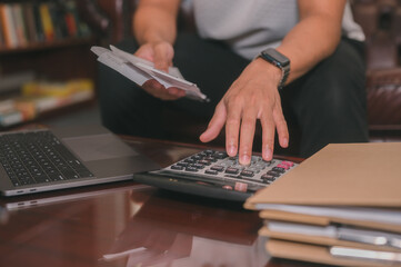 Business accounting concept, Business man using calculator with computer laptop, budget and loan paper in office, Unrecognizable person counting expenses on calculator