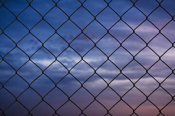 Fototapeta premium Old metal wire fence rust on the purple and blue sky background there are many clouds.