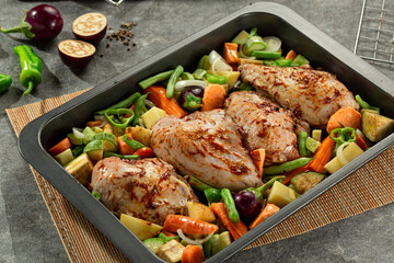 Tray of raw marinated chicken breast with vegetables.