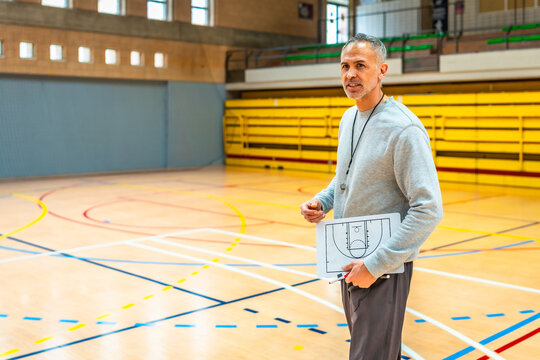 Basketball coach holding tactical board explaining game strategy in gym