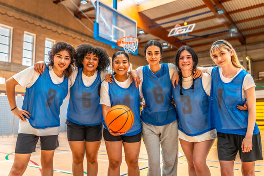 Female basketball team smiling and embracing in gymnasium