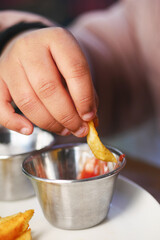 Hand dipping fry in ketchup at a diner table