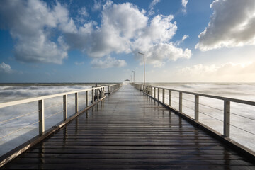 Obraz premium Henley jetty, Adelaide South Australia, long exposure ocean waves with timber jetty extending into distance, dramatic clouds in blue sky