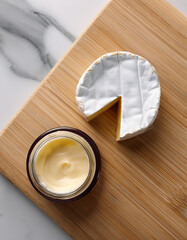 A luxury face cream jar placed beside a piece of Brie cheese on a marble surface, soft natural lighting, minimalist aesthetic, skincare product photography