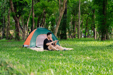 Person enjoying a quiet moment reading a book outside a colorful tent in a green forest on a sunny...