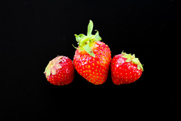 Red strawberries with green stems stand out against a dark, almost black background. This simple...