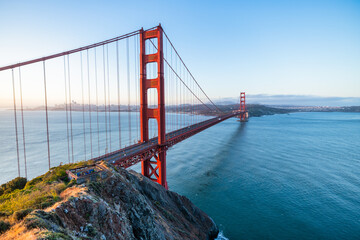 Golden Gate Bridge at sunrise in San Francisco, California. Scenic view from Battery Spencer with soft pastel sky, calm bay waters, and iconic red architecture. Tranquil travel landscape.