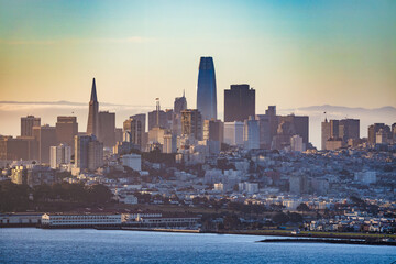 Downtown San Francisco skyline view with iconic Transamerica Pyramid and Salesforce Tower. Overcast sky, dense urban architecture, and waterfront buildings captured from a high vantage point.