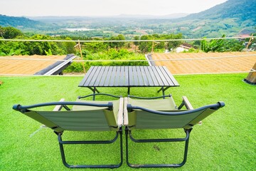 Two green lounge chairs on a grassy terrace overlooking a scenic valley and mountains under a...