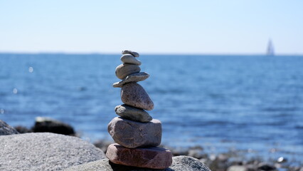 Pebbles carefully balanced on the shore with the blue sea in the background.

